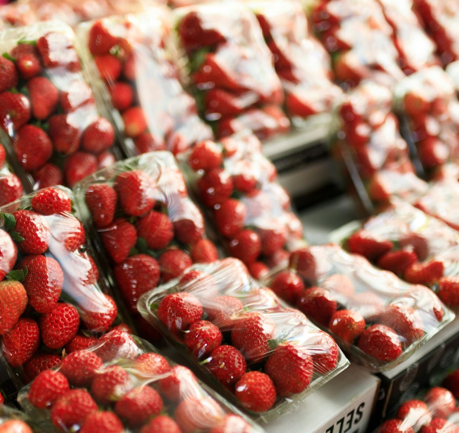 Fresh strawberries in transparent plastic packaging displayed in a market setting.